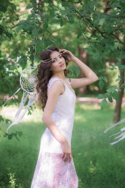Güzel bir saç modeli ile uzun beyaz elbiseli genç çekici kız, bir yaz parkında beyaz rüya yakalayıcılar ile