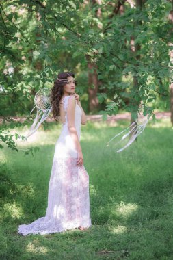 Güzel bir saç modeli ile uzun beyaz elbiseli genç çekici kız, bir yaz parkında beyaz rüya yakalayıcılar ile