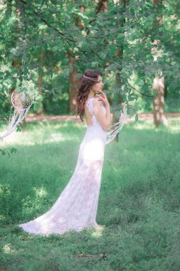 Güzel bir saç modeli ile uzun beyaz elbiseli genç çekici kız, bir yaz parkında beyaz rüya yakalayıcılar ile