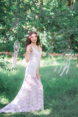 Güzel bir saç modeli ile uzun beyaz elbiseli genç çekici kız, bir yaz parkında beyaz rüya yakalayıcılar ile
