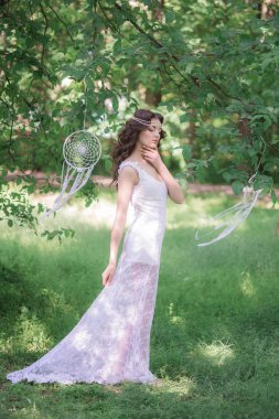 Güzel bir saç modeli ile uzun beyaz elbiseli genç çekici kız, bir yaz parkında beyaz rüya yakalayıcılar ile