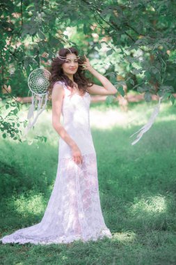 Güzel bir saç modeli ile uzun beyaz elbiseli genç çekici kız, bir yaz parkında beyaz rüya yakalayıcılar ile