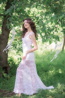 Güzel bir saç modeli ile uzun beyaz elbiseli genç çekici kız, bir yaz parkında beyaz rüya yakalayıcılar ile