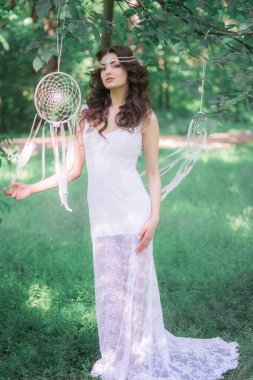 Güzel bir saç modeli ile uzun beyaz elbiseli genç çekici kız, bir yaz parkında beyaz rüya yakalayıcılar ile