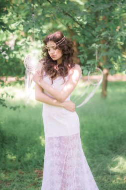 Güzel bir saç modeli ile uzun beyaz elbiseli genç çekici kız, bir yaz parkında beyaz rüya yakalayıcılar ile