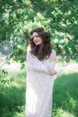 Güzel bir saç modeli ile uzun beyaz elbiseli çekici genç kız, bir yaz parkında beyaz dantel vintage eşarp ile