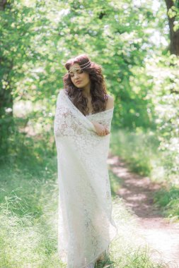 Güzel bir saç modeli ile uzun beyaz elbiseli çekici genç kız, bir yaz parkında beyaz dantel vintage eşarp ile