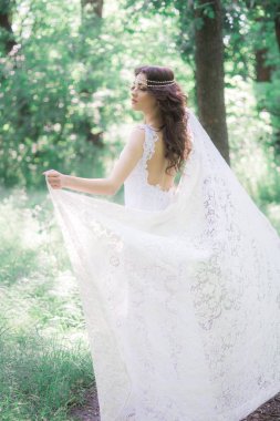 Güzel bir saç modeli ile uzun beyaz elbiseli çekici genç kız, bir yaz parkında beyaz dantel vintage eşarp ile