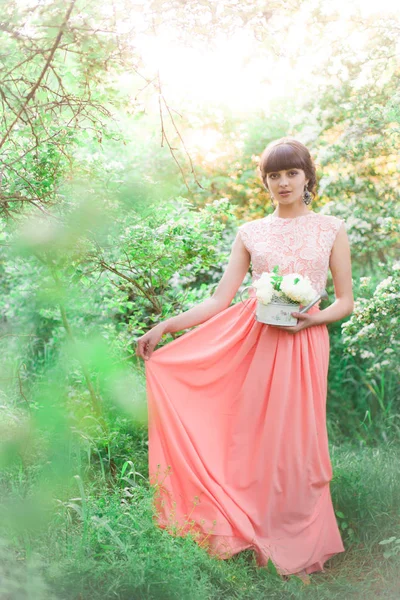 日没時の夏の公園で彼女の手に白い花を持つ長いドレスを着た若い魅力的な女の子 — ストック写真