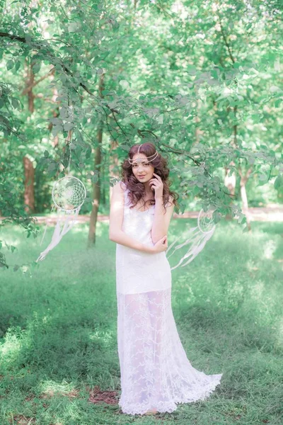 Güzel bir saç modeli ile uzun beyaz elbiseli genç çekici kız, bir yaz parkında beyaz rüya yakalayıcılar ile