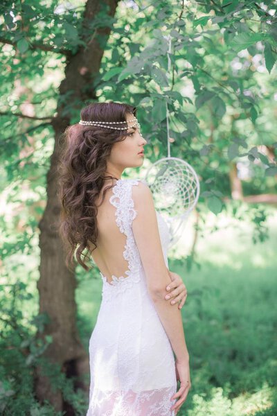 Young attractive girl in a long white dress with a beautiful hairstyle, with white dream catchers in a summer park