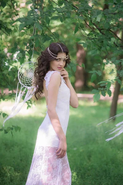 年轻的有吸引力的女孩在一个长白色礼服与美丽的发型 与白色梦想捕手在夏天公园 — 图库照片