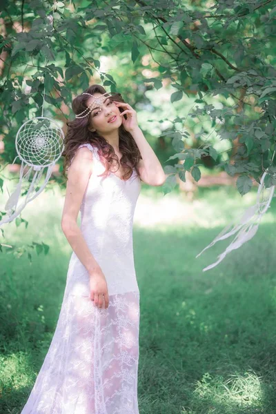年轻的有吸引力的女孩在一个长白色礼服与美丽的发型 与白色梦想捕手在夏天公园 — 图库照片