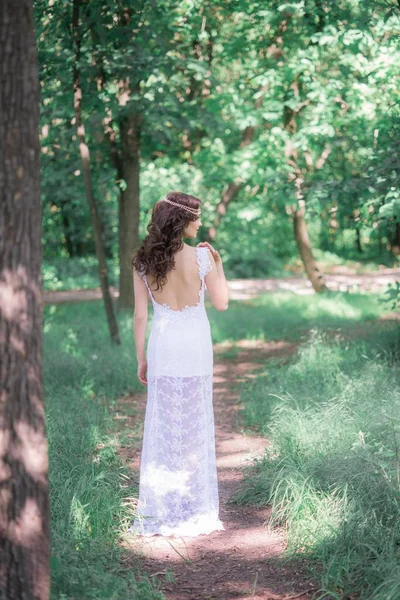 迷人的年轻女孩在一个长长的白色礼服与美丽的发型在夏天公园 — 图库照片