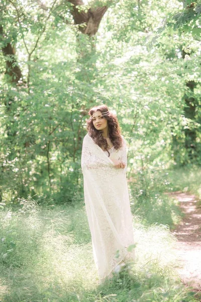 迷人的年轻女孩在一个长长的白色连衣裙与美丽的发型 与白色蕾丝复古围巾在夏季公园 — 图库照片