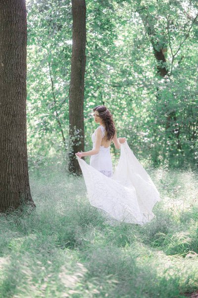 Attractive young girl in a long white dress with a beautiful hairstyle, with a white lace vintage scarf in a summer park