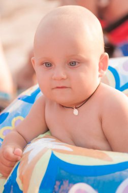 Küçük yürümeye başlayan çocuk mavi şişme halka plajda oturan