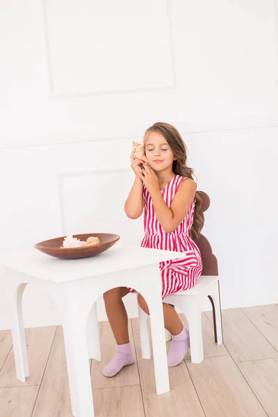 可爱的女孩在一个美丽的礼服在家里玩在儿童表与贝壳 — 图库照片