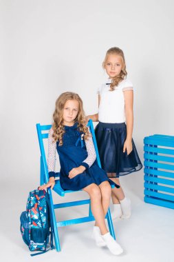 Beyaz bir arka plan üzerinde mavi sandalye ile bir sırt çantası, kitap ve defterler ile güzel bir trendy okul üniforması iki sevimli kız öğrenciler