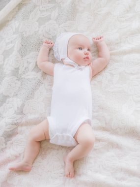 Beyaz giysiler içinde Sevimli yürümeye başlayan bebek evde beyaz bir yatakta yatıyor