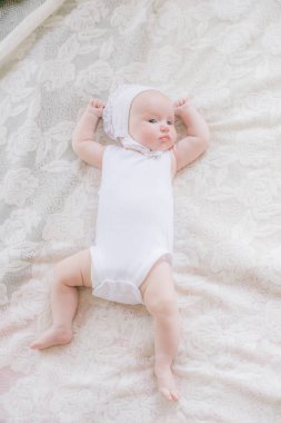 Beyaz giysiler içinde Sevimli yürümeye başlayan bebek evde beyaz bir yatakta yatıyor