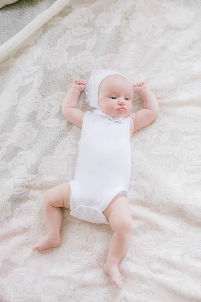 白い服を着たかわいい幼児の赤ちゃんは 自宅で白いベッドの上に横たわっています — ストック写真