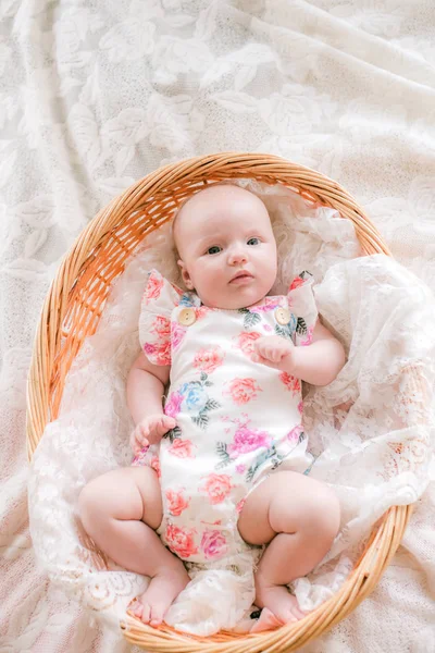 花柄の服を着たかわいい赤ちゃんの赤ちゃんは 自宅の白いベッドの上にウィッカーバスケットに横たわっています — ストック写真