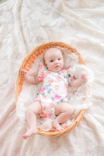 花柄の服を着たかわいい赤ちゃんの赤ちゃんは 自宅の白いベッドの上にウィッカーバスケットに横たわっています — ストック写真