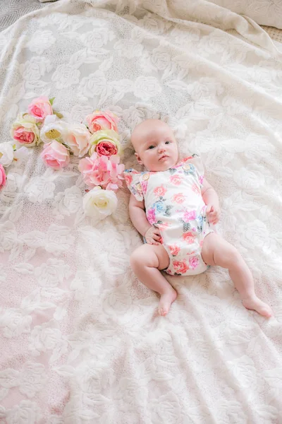 小さなかわいい女の子は 花の花のボディスーツで 自宅の白いベッドに横たわっています 幸せな健康な母性 — ストック写真