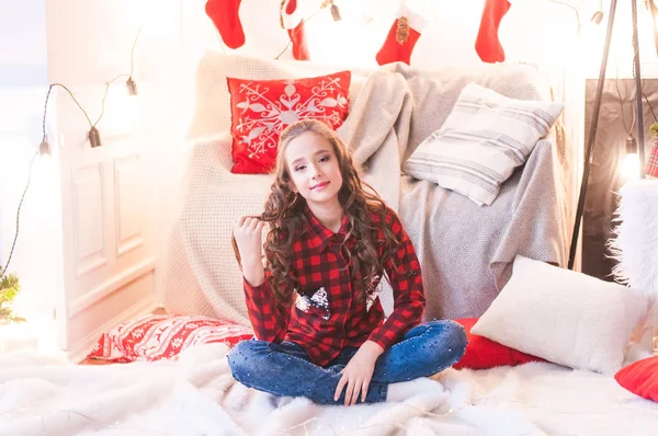 Cute girl in a red checkered shirt at home in the room decorated for Christmas. Happy christmas mood