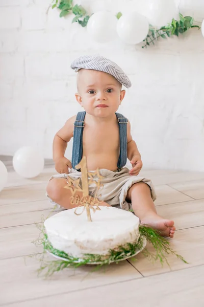 サスペンダーとヴィンテージキャップの小さなかわいい男の子 誕生日ケーキと白い風船とユーカリの小枝と装飾と最初の誕生日 素朴な最初の誕生日パーティー — ストック写真