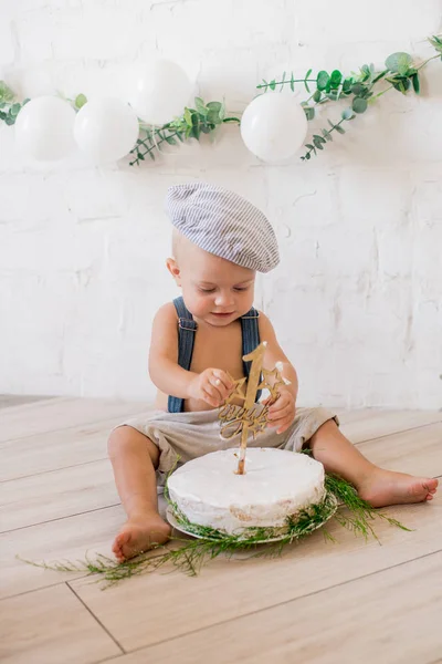 小可爱的男孩在吊带和复古帽 生日一周 生日蛋糕和装饰与白色气球和枝花的紫杉 生锈的第一个生日派对 — 图库照片