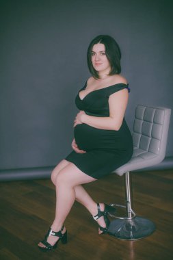 Modaya uygun bir gece elbisesi içinde koyu saçlı genç hamile kız. Hamile kadınlar için şık giysiler.