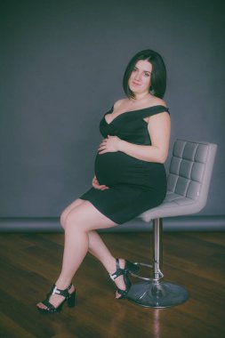 Modaya uygun bir gece elbisesi içinde koyu saçlı genç hamile kız. Hamile kadınlar için şık giysiler.