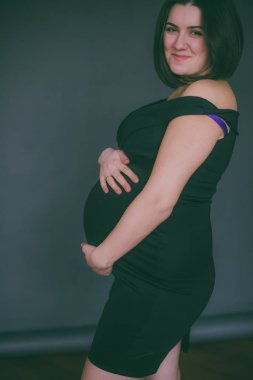 Modaya uygun bir gece elbisesi içinde koyu saçlı genç hamile kız. Hamile kadınlar için şık giysiler.