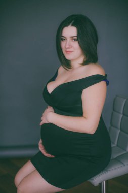 Modaya uygun bir gece elbisesi içinde koyu saçlı genç hamile kız. Hamile kadınlar için şık giysiler.