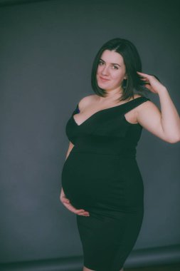 Modaya uygun bir gece elbisesi içinde koyu saçlı genç hamile kız. Hamile kadınlar için şık giysiler.