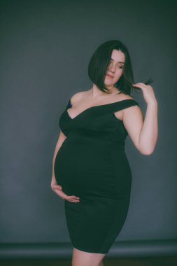 Modaya uygun bir gece elbisesi içinde koyu saçlı genç hamile kız. Hamile kadınlar için şık giysiler.