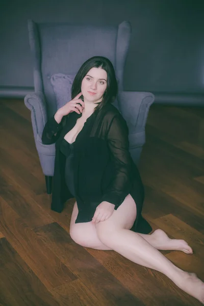 Young pregnant woman with dark hair in black lingerie and a black silk shirt on a dark background