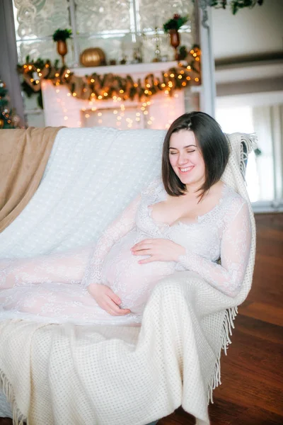Mladá Těhotná Dívka Tmavými Vlasy Bílých Šatech Pohovce Vánočním Prostředí — Stock fotografie