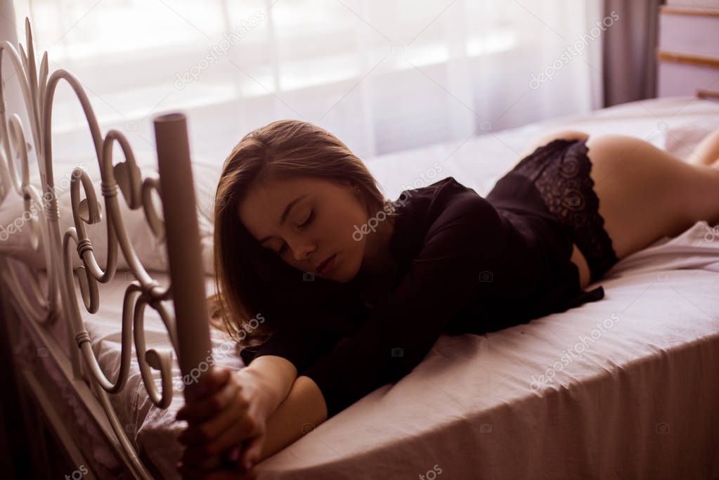 Young attractive girl with long dark hair in lace black lingerie and a black silk shirt on the bed. Boudoir photo of a young girl