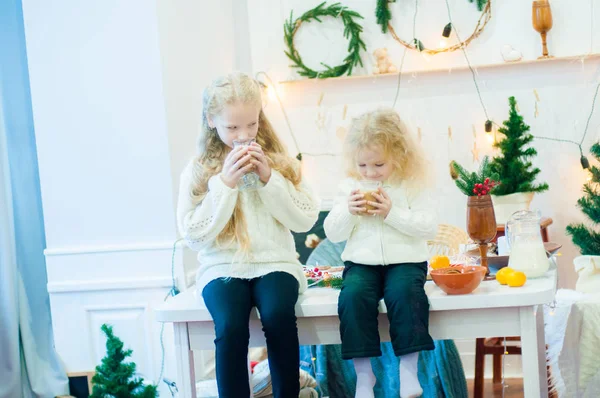 Dvě Roztomilá Sestřičky Blonďatými Kudrnatými Vlasy Vánočním Stole Pijou Kakao — Stock fotografie