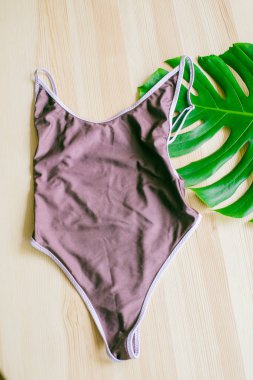 Tropikal yeşil yapraklı, ahşap bir arka planda parlak moda bikini. Modaya uygun plaj kıyafeti..