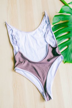 Tropikal yeşil yapraklı, ahşap bir arka planda parlak moda bikini. Modaya uygun plaj kıyafeti..