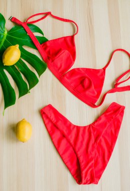 Sarı limonlu ve tropikal yeşil yapraklı ahşap bir arka planda parlak moda bikini. Modaya uygun plaj kıyafeti..