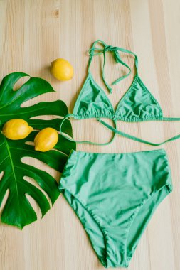 Sarı limonlu ve tropikal yeşil yapraklı ahşap bir arka planda parlak moda bikini. Modaya uygun plaj kıyafeti..