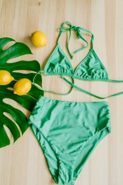 Sarı limonlu ve tropikal yeşil yapraklı ahşap bir arka planda parlak moda bikini. Modaya uygun plaj kıyafeti..
