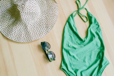 Ahşap arka planda parlak moda bikiniler ve geniş kenarlı ve güneş gözlüklü bir hasır şapka. Modaya uygun plaj giysileri ve aksesuarları..