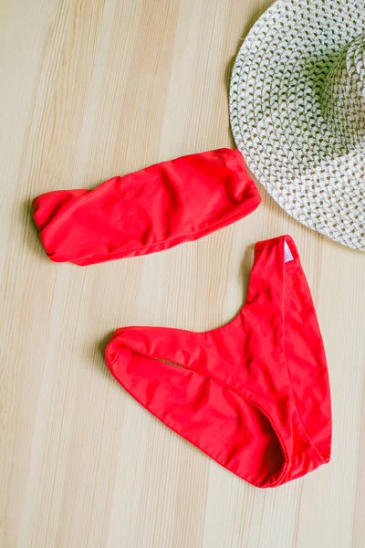 Bright trendy bikinis on a wooden background, as well as a straw hat with wide brim and sunglasses. Fashionable beachwear and accessories.