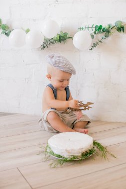 İlk doğum gününde beyaz balonlar ve klasik kıyafetlerle doğum günü pastası olan sevimli küçük bir çocuk.